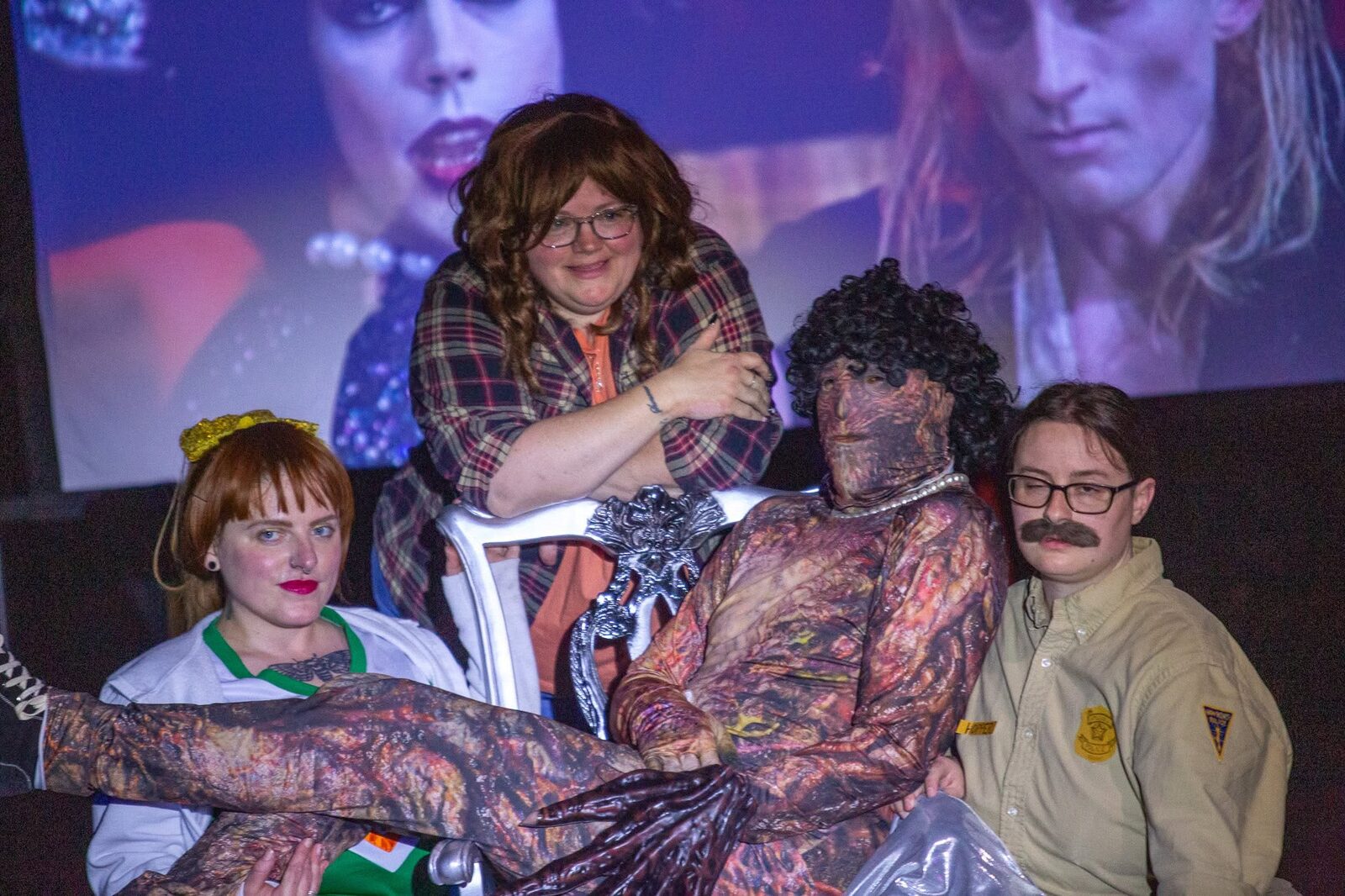 Cast members posed together on a silver chair